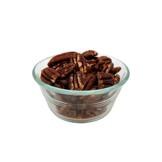 A clear glass bowl filled with unsalted pecans on a light gray studio background.