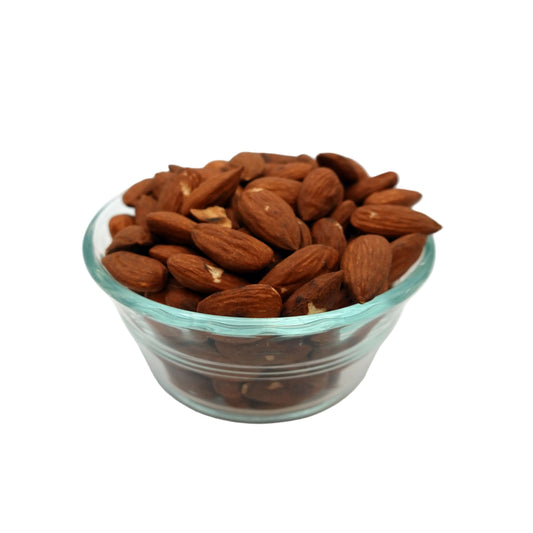 A clear glass bowl filled with whole unsalted almonds on a light gray studio background.