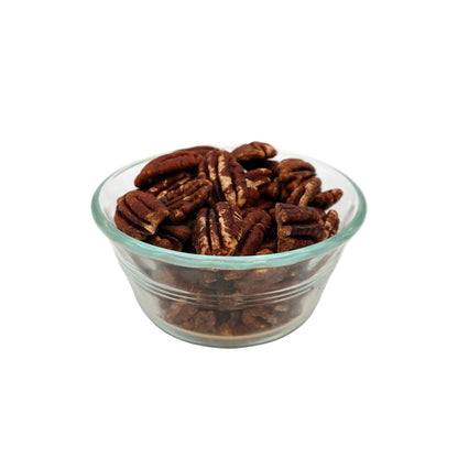 A clear glass bowl filled with unsalted pecans on a light gray studio background.