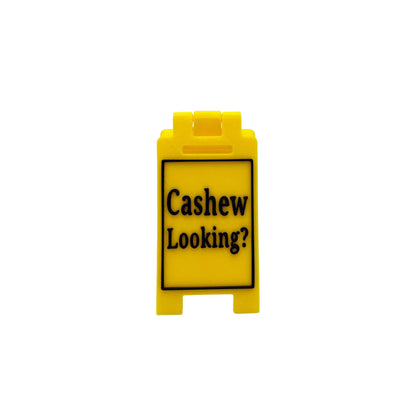 A small yellow plastic sign with black text reading 'Cashew Looking?' on a light gray background.