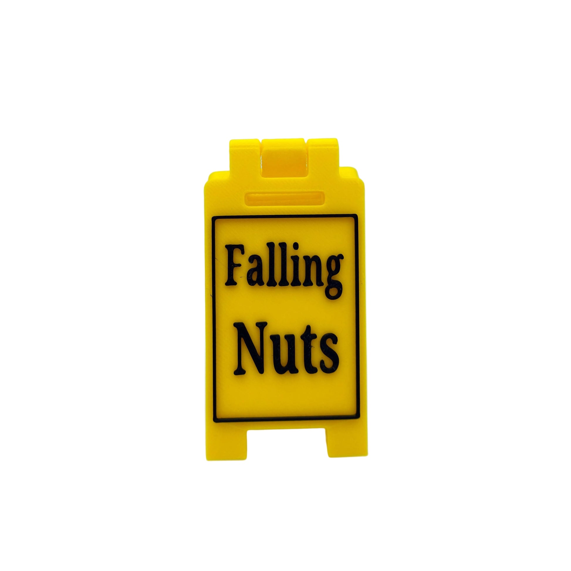 A small yellow plastic sign with black text reading 'Falling Nuts' on a white studio background.