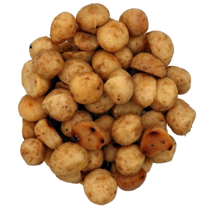 A top-down view of roasted salted macadamias in a clear glass bowl on a white background.