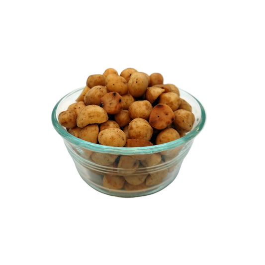 A clear glass bowl filled with small roasted salted macadamias, photographed on a plain white studio background.