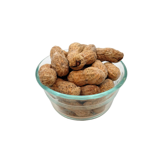A clear glass bowl filled with salted in-shell peanuts in their shells, photographed on a plain light background.