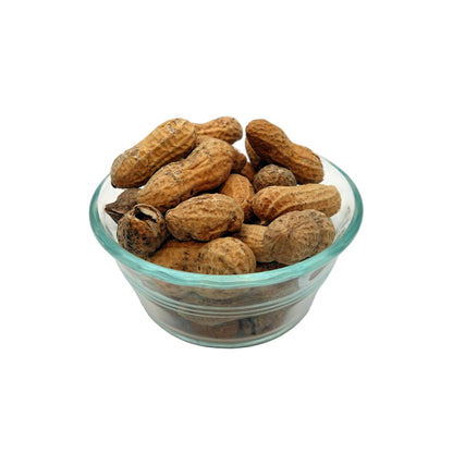 A small clear glass bowl filled with unsalted in-shell peanuts in their natural brown shells, set against a seamless light gray studio background.