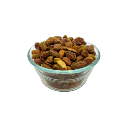 A small clear glass bowl filled with roasted pistachios on a white studio background.