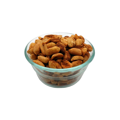 Roasted old bay cashews piled in a small clear glass bowl on a light gray studio background.