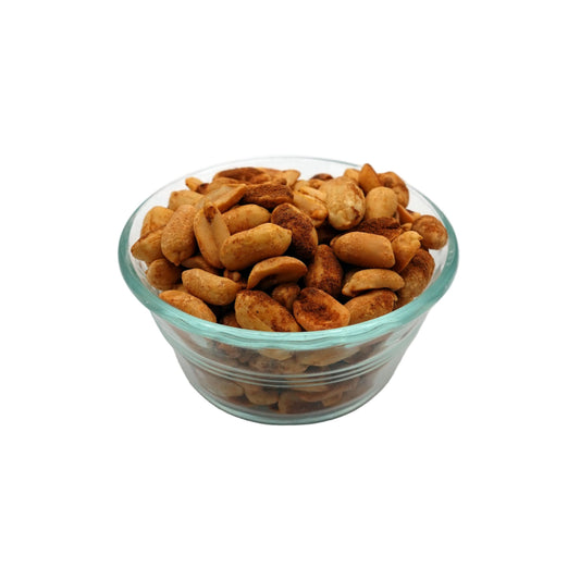 Roasted old bay cashews piled in a small clear glass bowl on a light gray studio background.