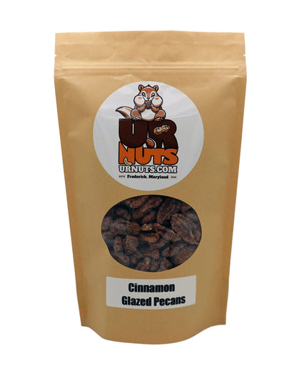 A stand-up kraft paper pouch of UR Nuts Cinnamon Glazed Pecans, featuring a circular logo with a cartoon nut logo and a clear window showing the brown glazed pecans inside.