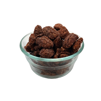 A small clear glass bowl filled with cinnamon glazed pecans, photographed on a plain light gray studio background.