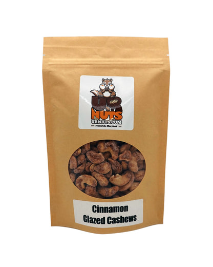A stand-up kraft paper pouch of 'Cinnamon Glazed Cashews' by UR Nuts, featuring a circular clear window showing the cashews inside and a cartoon raccoon logo on the front.