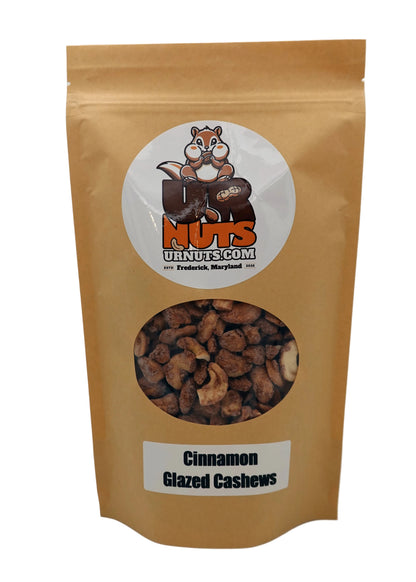 A stand-up kraft paper pouch of Cinnamon Glazed Cashews from UR Nuts, featuring a circular logo with a cartoon nut logo and a clear window showing the cashews inside.