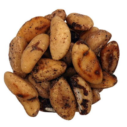 Roasted brazil nuts in a clear glass bowl, photographed from a top-down view on a plain white background.