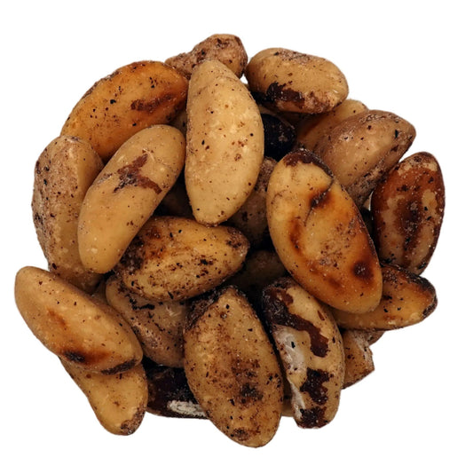 Roasted brazil nuts in a clear glass bowl, photographed from a top-down view on a plain white background.