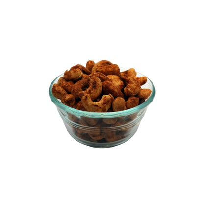 A clear glass bowl filled with old bay cashews, photographed on a plain light gray studio background.